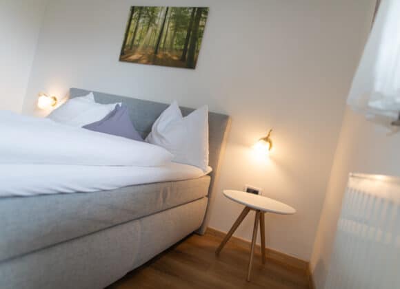 Modernes Zimmer mit klaren Linien und hellen Farben in der Pension Klausthaler, Mölten, Südtirol. Die großen Fenster lassen viel Licht herein und bieten Ausblicke auf die Berge.